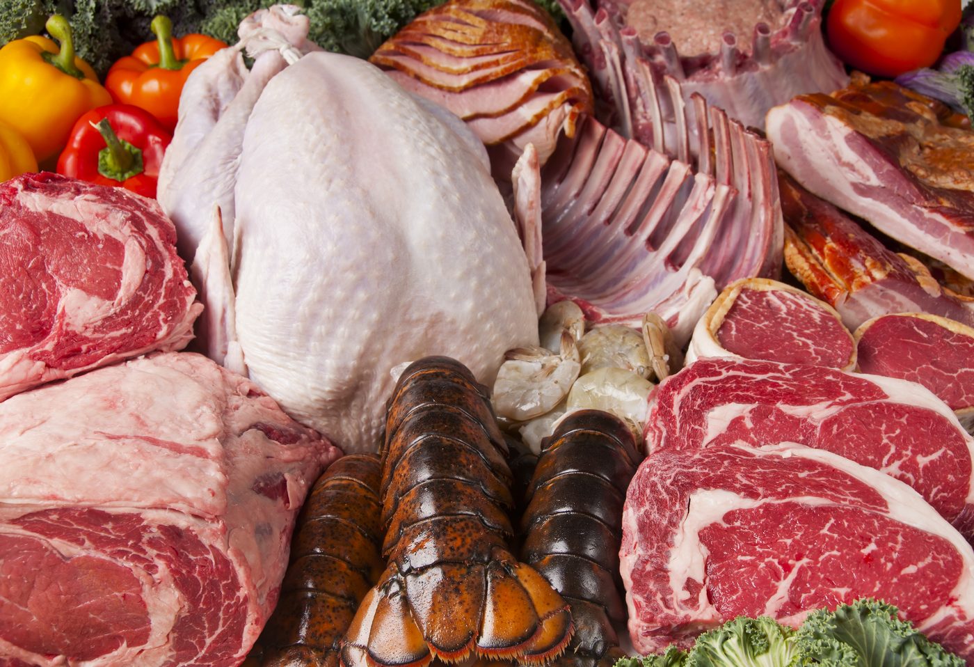 An assortment of steaks, a whole turkey, a rack of lamb, ham, bacon, lobster tails and shrimp.